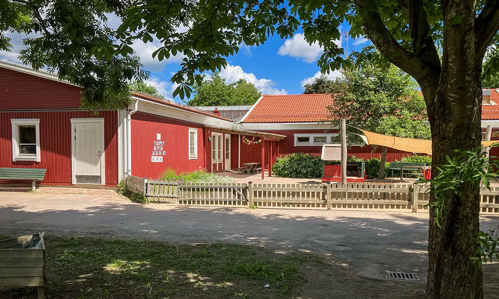 Foto av Gröngarns förskola. Det är en röd träbyggnad med vita knutar.