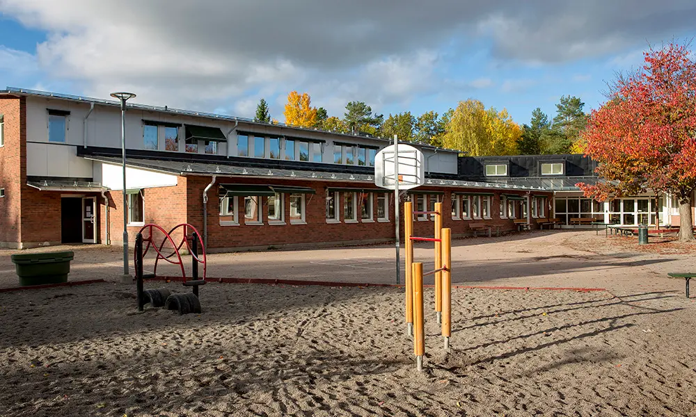 Foto av Bergvretenskolan. Det är en flervåningsbyggnad i tegel. I förgrunden av bilden syns en del av skolgården.