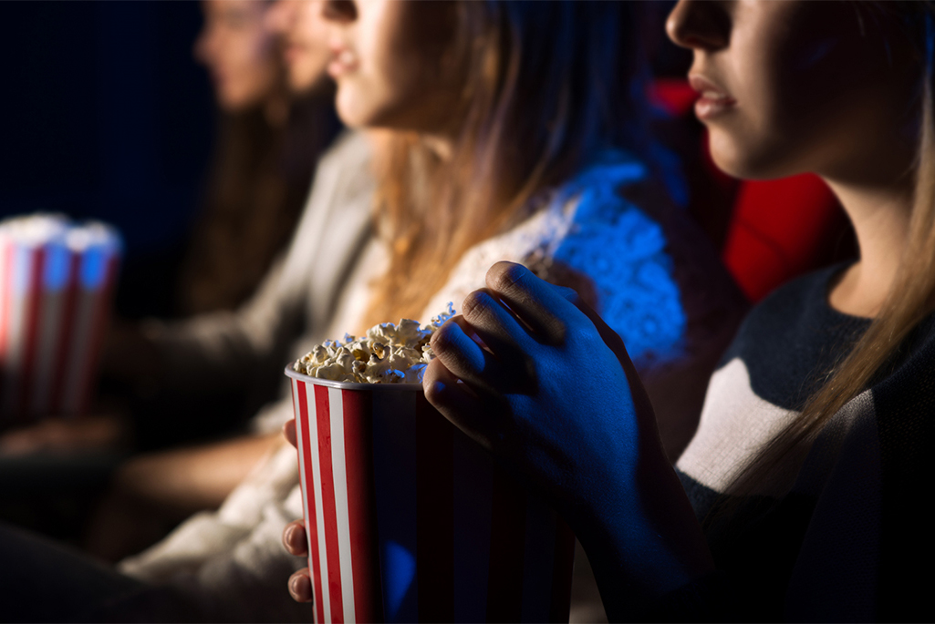 Foto på unga människor som äter popcorn i en biosalong. 