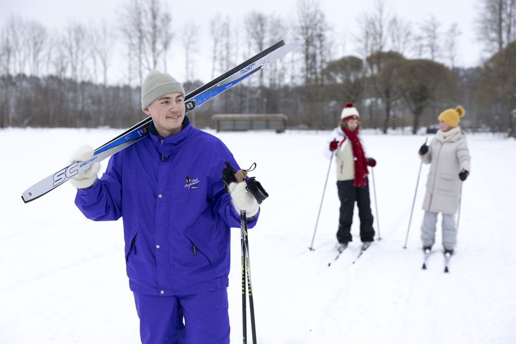 Två personer som åker skidor utomhus i snön och en person som håller i sina skidor.